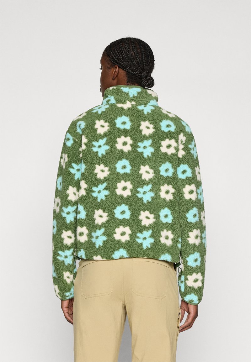 Giacca in pile verde con motivo floreale in azzurro chiaro e bianco. Presenta un colletto alto e un taglio corto. Texture distintiva e morbida.