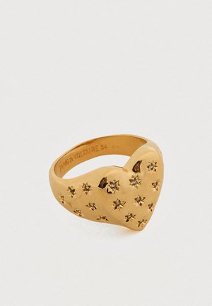 Gouden hartvormige ring met veelpuntige sterpatronen en kleine accenten. Soepele textuur, iets dikkere ringband met gegraveerd merkteken.