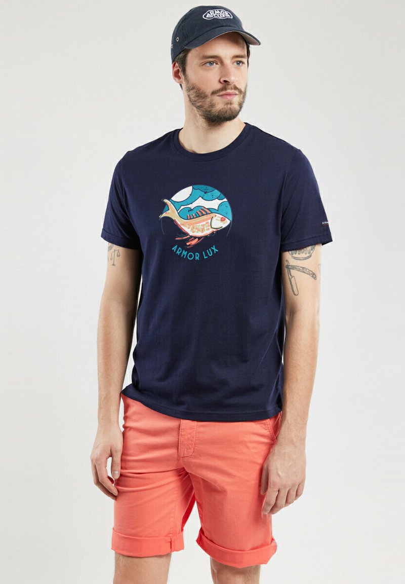 T-shirt en coton bleu marine avec un design graphique de poisson, associé à un short coral clair, avec des manches retroussées et cinq poches.