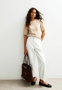 Beige gebreide trui, witte hoge taillebroek, zwarte ballerina's en een bruine suède handtas met zilveren accenten, tegen een neutrale achtergrond.