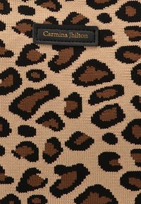 Tejido con estampado de leopardo que presenta manchas negras y marrones sobre un fondo beige, con una etiqueta negra que dice "Carmina Jhilton" en letras doradas.