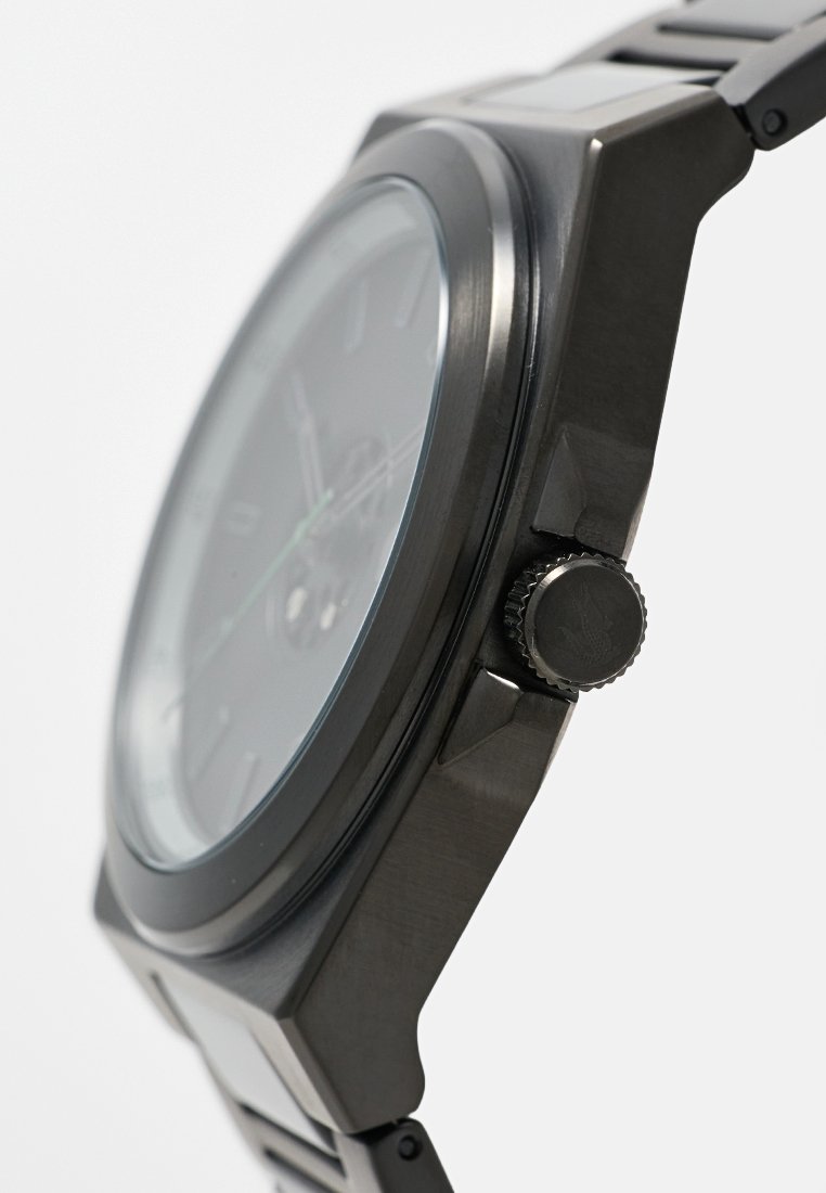 Primer plano de un reloj de pulsera negro de metal que muestra la corona lateral, el bisel redondo y la pulsera enlazada sobre un fondo blanco.