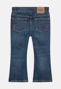 Blå denim jeans med utsvängda ben och midjehöjd, med två bakfickor, kontrasterande orange sömnad och en logotyp vid midjan.