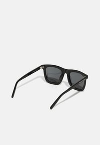 Black sunglasses with a rectangular frame, dark lenses, shiny plastic material, and straight temples featuring subtle branding on the arm.