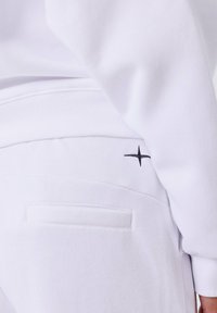 Witte sweatshirt met een gestructureerde afwerking, met een zwarte geborduurde sterdetail boven een zak op de achterkant. Eenvoudig, schoon ontwerp.