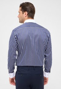 Camicia a righe blu navy con strisce verticali bianche, maniche lunghe e colletto bianco. Presenta polsini con bottoni e vestibilità slim.