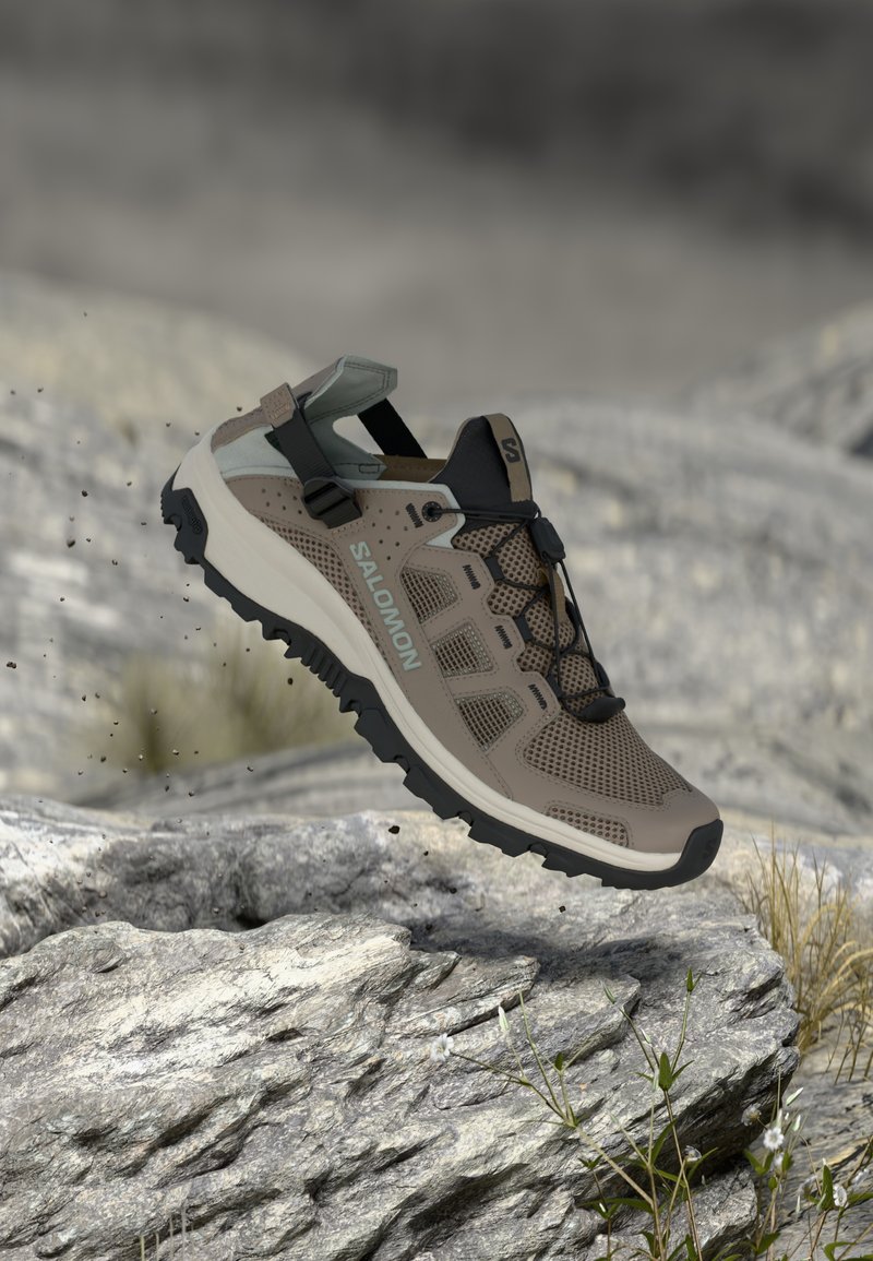 Ελαφρύ πεζοπορικό παπούτσι σε ταμπά χρώμα με επάνω μέρος από δίχτυ, μαύρες λεπτομέρειες και υφασμένο λαστιχένιο πάτο. Διαθέτει ρυθμιζόμενο λουράκι και λαβές πρόσφυσης για καλύτερο κράτημα.