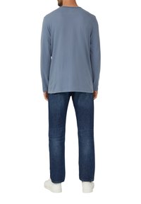 Blauwe katoenen T-shirt met lange mouwen, rechte snit, ronde hals, gedragen met donkerdenim jeans en witte sneakers, gezien van achteren.