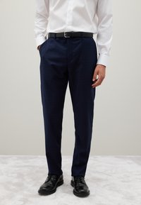 Pantalones de vestir azul marino con un sutil patrón de cuadros, ajuste entallado, textura suave, combinados con un cinturón negro y zapatos negros.