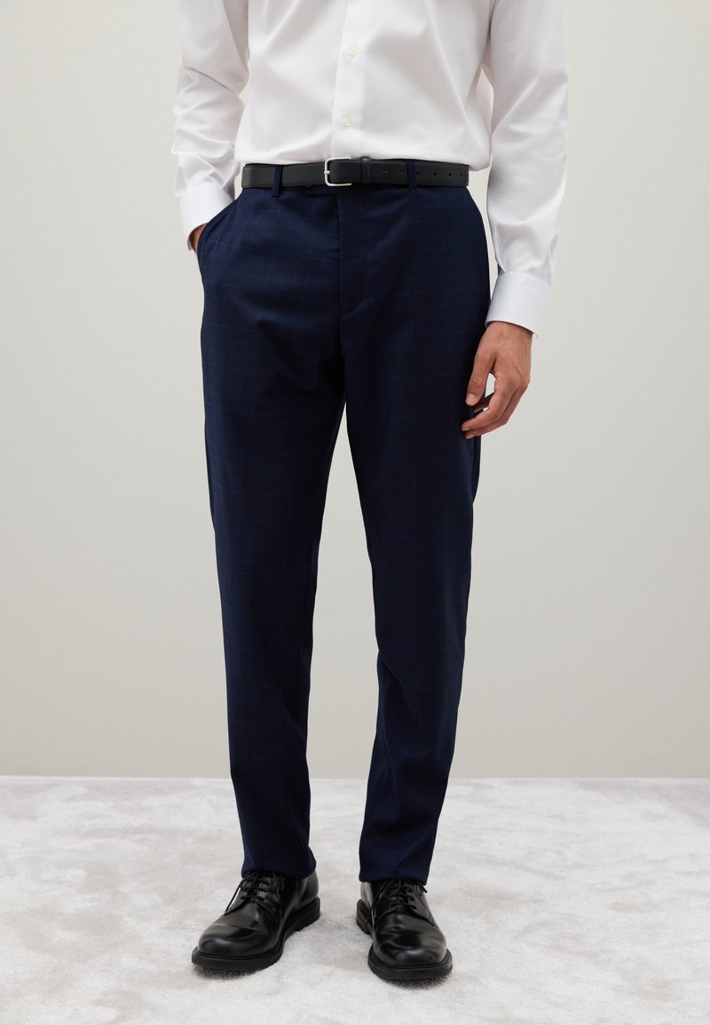 Pantalones de vestir azul marino con un sutil patrón de cuadros, ajuste entallado, textura suave, combinados con un cinturón negro y zapatos negros.