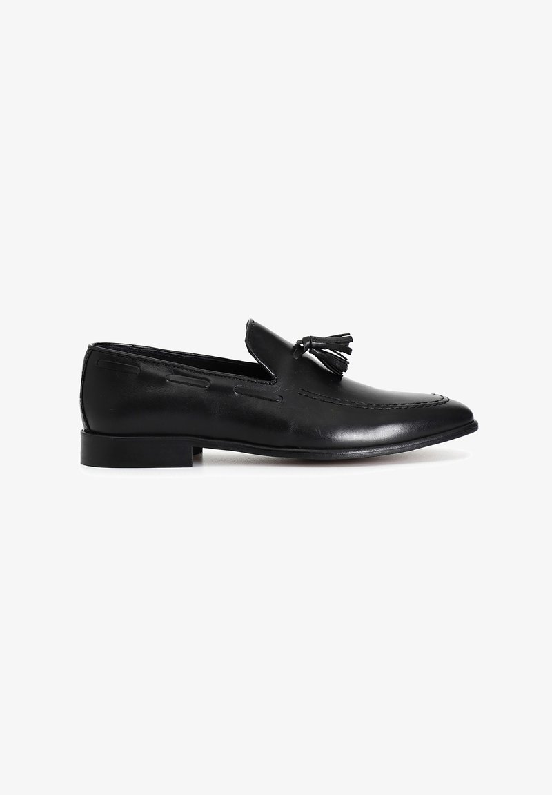 Mocasines de cuero negro con un diseño con borlas, textura suave, suela plana y una forma de punta afilada y elegante.