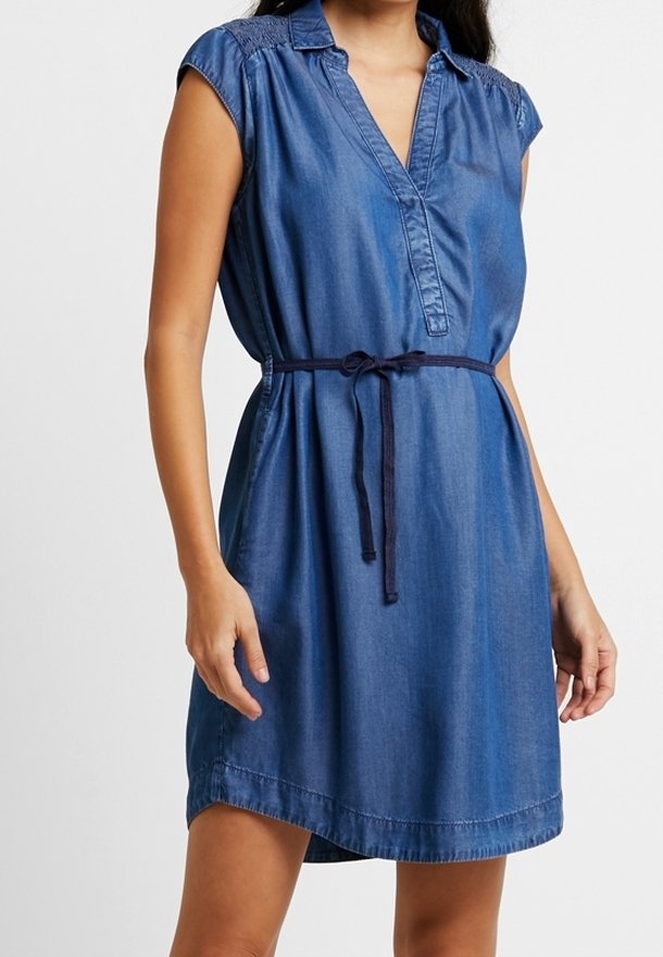 Džínové šaty s mělkým límcem, krátkými rukávy a zavázaným pasem. Mají hladkou texturu a jednolitou tmavě modrou barvu.