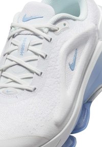 Fehér sportcipő texturált felső résszel, világoskék részletekkel, fűzős záródással és látható párnázottsággal a sarkán. A Nike márkajelzés is megtalálható rajta.