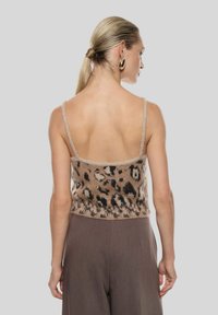Top corto lavorato a maglia con stampa leopardata, dotato di spalline regolabili, in tonalità marrone e nero; abbinato a pantaloni marroni a vita alta.