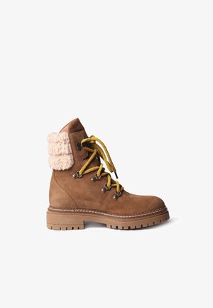 Bottine en daim marron avec un bord en laine crème texturée, des lacets jaunes, des œillets métalliques et une semelle en caoutchouc robuste.