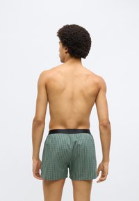 Zöld kockás boxeralsó fekete elasztikus derékpánttal, normál szabással és könnyű anyagból, hátulról nézve.