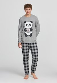 Maglietta grigia a maniche lunghe con grafica di panda e testo "MA PRIMA IL Caffè", abbinata a pantaloni a quadri neri e grigi, in materiale cotone.