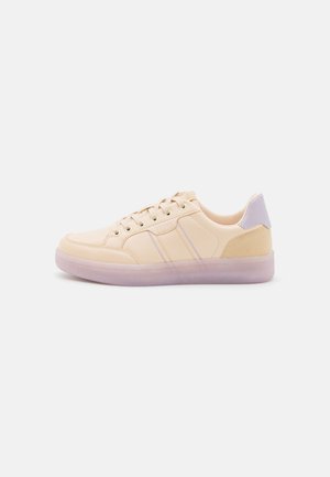 Beige sneakers with a smooth leather upper, subtle lilac accents, two decorative stripes, and a clear rubber sole. Low-profile design.