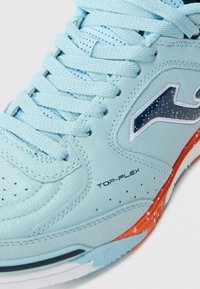 Scarpa sportiva azzurro chiaro con tomaia in pelle liscia, texture perforata, dettagli arancioni sulla suola e il logo nero.
