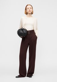 Κρεμ ζακέτα, λευκή ριμπ τοπ, μπορντό παντελόνι ψηλόμεσο με διπλό κούμπωμα και μαύρη στρογγυλή τσάντα. Λείες υφές, εφαρμοστός σχεδιασμός.