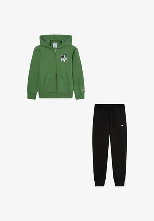 Grüne Zip-Hoodie mit Vordertasche und Astronauten-Graphic; kombiniert mit schwarzen Jogginghosen, die einen elastischen Bund und ein Logo aufweisen.