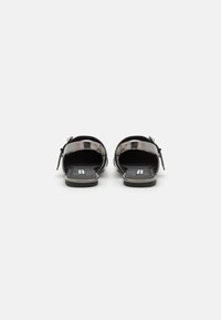 Sandalias deslizantes de látex negro con parte trasera abierta, diseño de doble tira y detalles de hebilla ajustable. Suela plana de goma con plantilla texturizada.