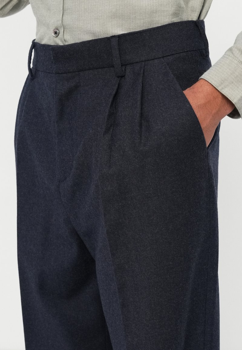 Dark navy trousers made of textured fabric, featuring a pleated front, side pockets, and a tailored waistband with belt loops.