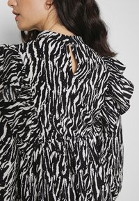 Blusa preta e branca com padrão, com mangas com volantes, apresentando um corte em forma de olho na parte de trás e cintura elástica para um melhor ajuste.