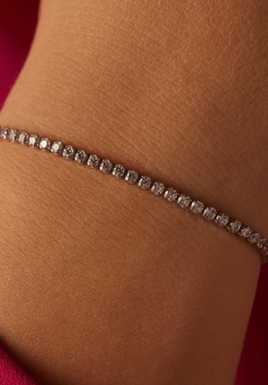 Zilveren armband met een doorlopende rij ronde, heldere stenen, rustend op een pols met een gestructureerde huid.