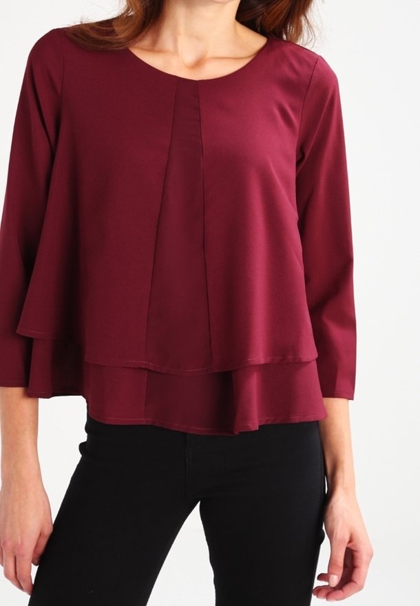 Blouse bordeaux en tissu lisse, avec un col rond, des manches trois-quarts et un design en couches avec des coutures délicates.