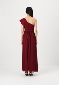Rochie maxi burgundă cu un umăr, cu un manșon volanat, talie strânsă și material fluid. Textură netedă și ușoară, cu fermoar ascuns.