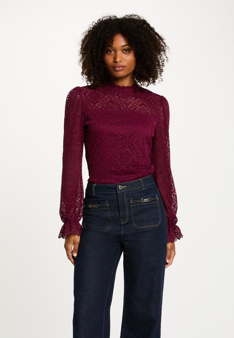 Top in pizzo bordeaux con maniche lunghe, scollatura a onda, motivo floreale, abbinato a jeans in denim scuro a vita alta con dettagli con zip.