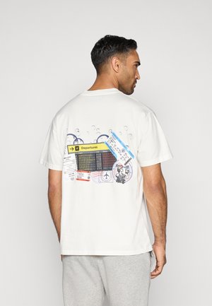 Camiseta de algodón blanca con un gráfico en la parte posterior que presenta varios billetes de viaje y un panel de salida, acentuado con gráficos de burbujas.