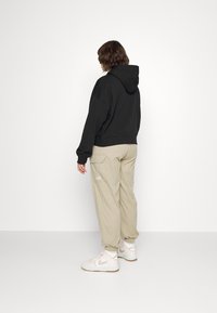 Sudadera negra con un corte relajado y capucha, combinada con pantalones cargo beige que tienen bolsillos, y zapatillas blancas con detalles en rosa.