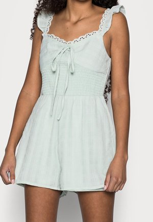 Lichtgroene romper met een smock-buste, ruffle schouderbanden en een kanten rand langs de halslijn; gemaakt van lichte, gestructureerde stof.