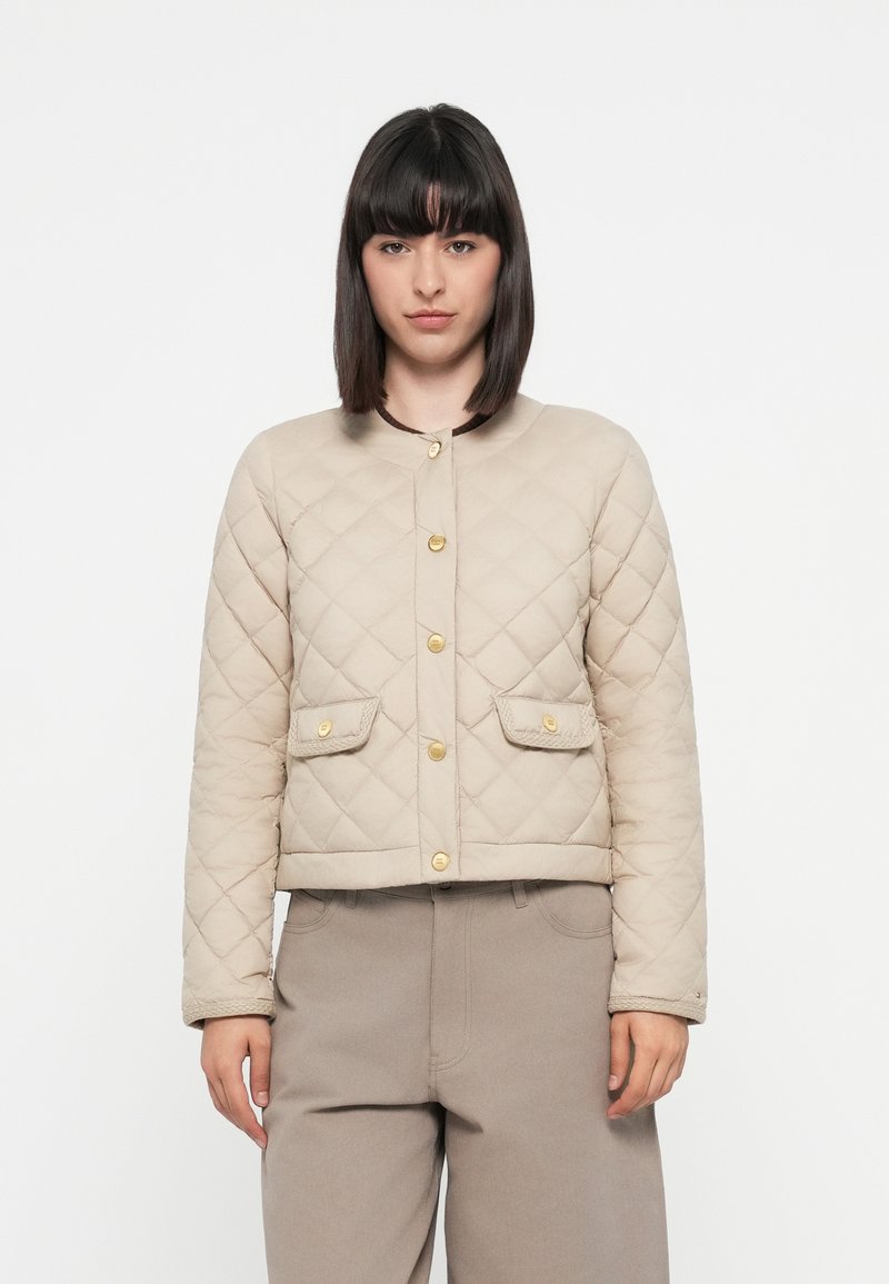 Beige quilted jacket with gold buttons, two front pockets, and a rounded neckline. Soft texture and cropped fit, paired with beige trousers.