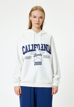 Biała bluza z kapturem z przodu z nadrukiem w ciemnoniebieskim kolorze "CALIFORNIA" oraz gwiazdą. Materiał wydaje się miękki, ma luźny krój i sznurki.