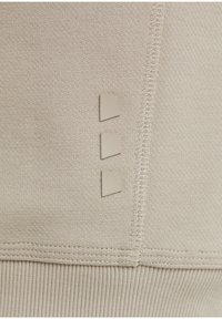 Béžová mikinová látka s texturovaným povrchem. Obsahuje tři malé obdélníkové záplaty připevněné vertikálně na straně.