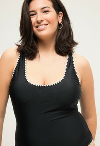 Černé plavky s kontrastním bílým trojúhelníkovým lemem podél výstřihu a ramínek, s hladkou texturou a přiléhavým střihem.