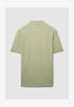 Polo vert clair en tissu texturé. Il présente un col classique avec une bordure blanche en accent sur le col et les manches.