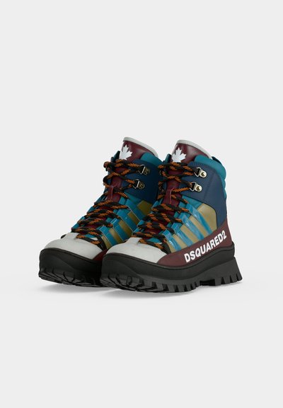 Paire de chaussures de randonnée multicolores avec semelles épaisses noires, lacets orange et noirs, marquage DSQUARED2 et feuille d'érable blanche sur la languette.