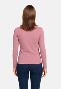 Maglietta a maniche lunghe, aderente, in morbido tessuto rosa, con una texture liscia e un collo rotondo. Abbinata a jeans aderenti di un blu scuro.