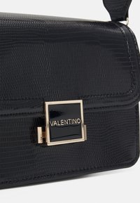 Black glossy handbag featuring a textured surface, gold-tone hardware, and a square logo accent on the front flap closure.