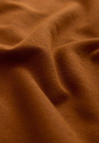 Ruda tekstūruota audinys banguotu paviršiumi, turi smulkų megztinį raštą ir švelnų blizgesį. Minkšta ir lanksti medžiaga.