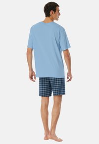 Hellblaues Baumwoll-T-Shirt kombiniert mit dunkelblau karierten Shorts. Die Shorts haben ein Rautenmuster mit weißen Linien und einem lockeren Sitz.