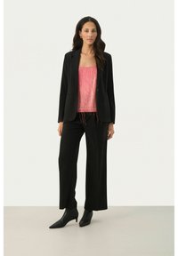 Sort skræddersyet blazer over en pink camisole med frynse detaljer, parret med brede sorte bukser og spidse sorte ankelstøvler.