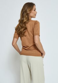 Krátký rukáv, přiléhavý svetr z jemné tan pleteniny s žebrovanými manžetami a lemem, kombinovaný s lehkými béžovými kalhotami s širokými nohavicemi. Texturovaná lehká tkanina.