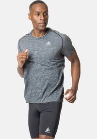 Grijs tekstuur kortemouwen sportshirt gecombineerd met zwarte strakke shorts, met een logo op het linkerbeen en gladde stof.