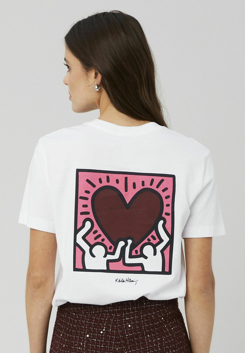 T-shirt en coton blanc avec un design graphique coloré au dos, comprenant un grand cœur et deux figures, entourées en noir.