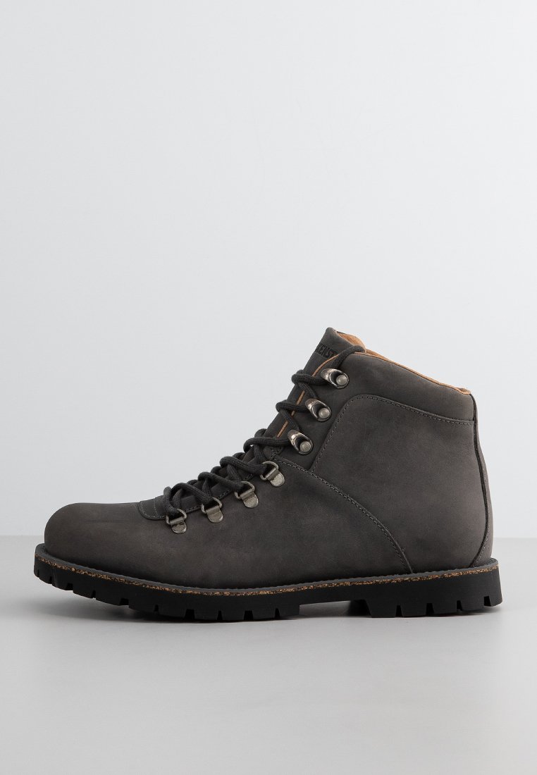 Botte de randonnée en cuir gris foncé avec des lacets noirs, œillets en métal, col rembourré et semelle épaisse à crampons sur une surface gris clair.